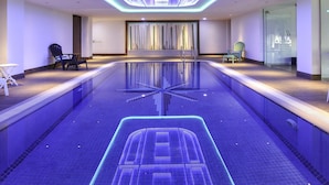 A modern indoor pool with a geometric light fixture above, two chairs, and a glass wall. - ibis Styles Dubai Jumeira (Dubai)