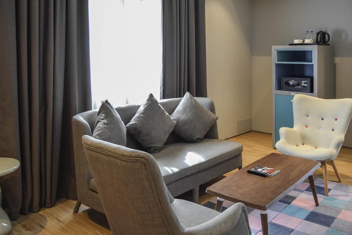 Una sala moderna con un sofá gris, un sillón blanco, una mesa de centro de madera y un mueble azul con microondas.