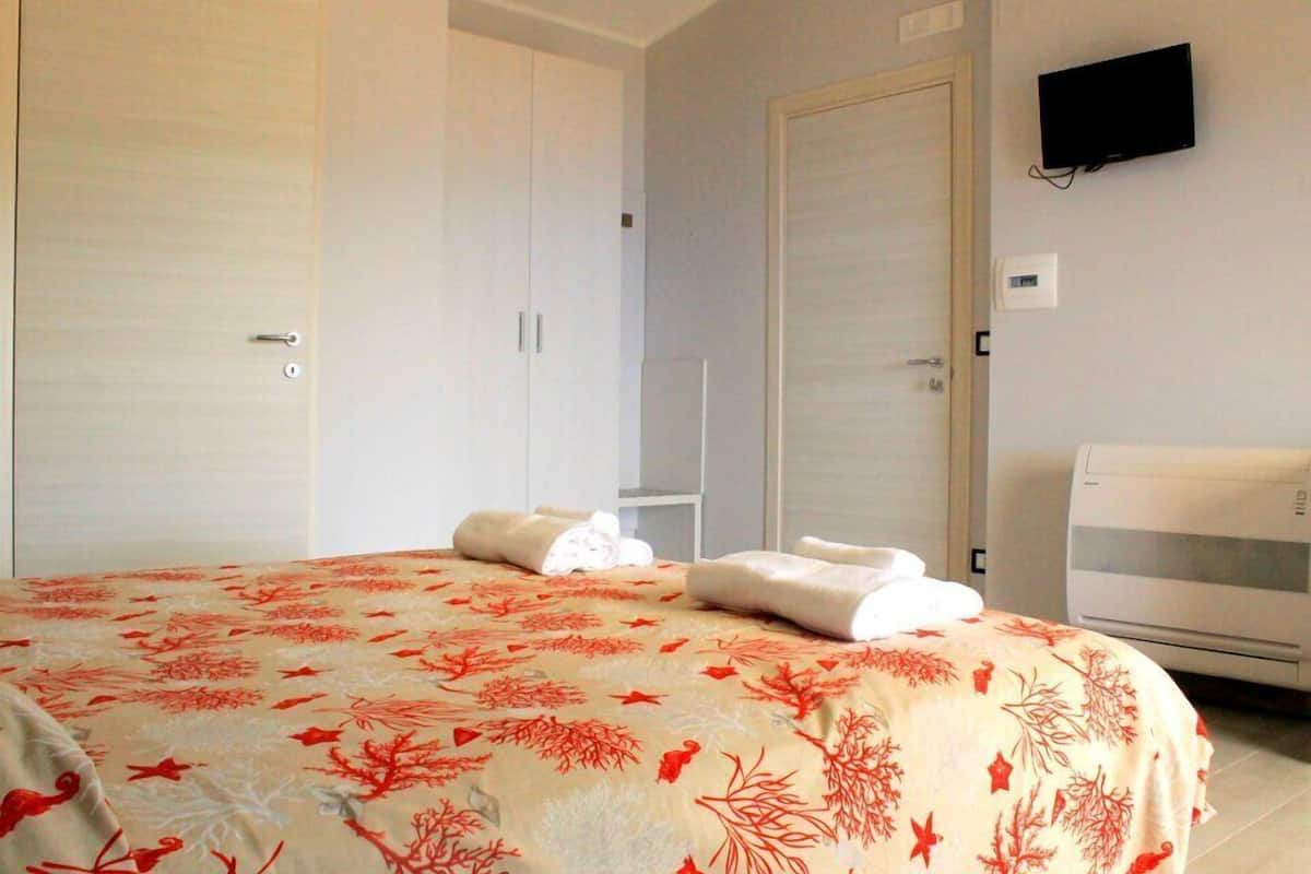 A hotel room with a bed, a TV mounted on the wall, and a thermostat on the wall.