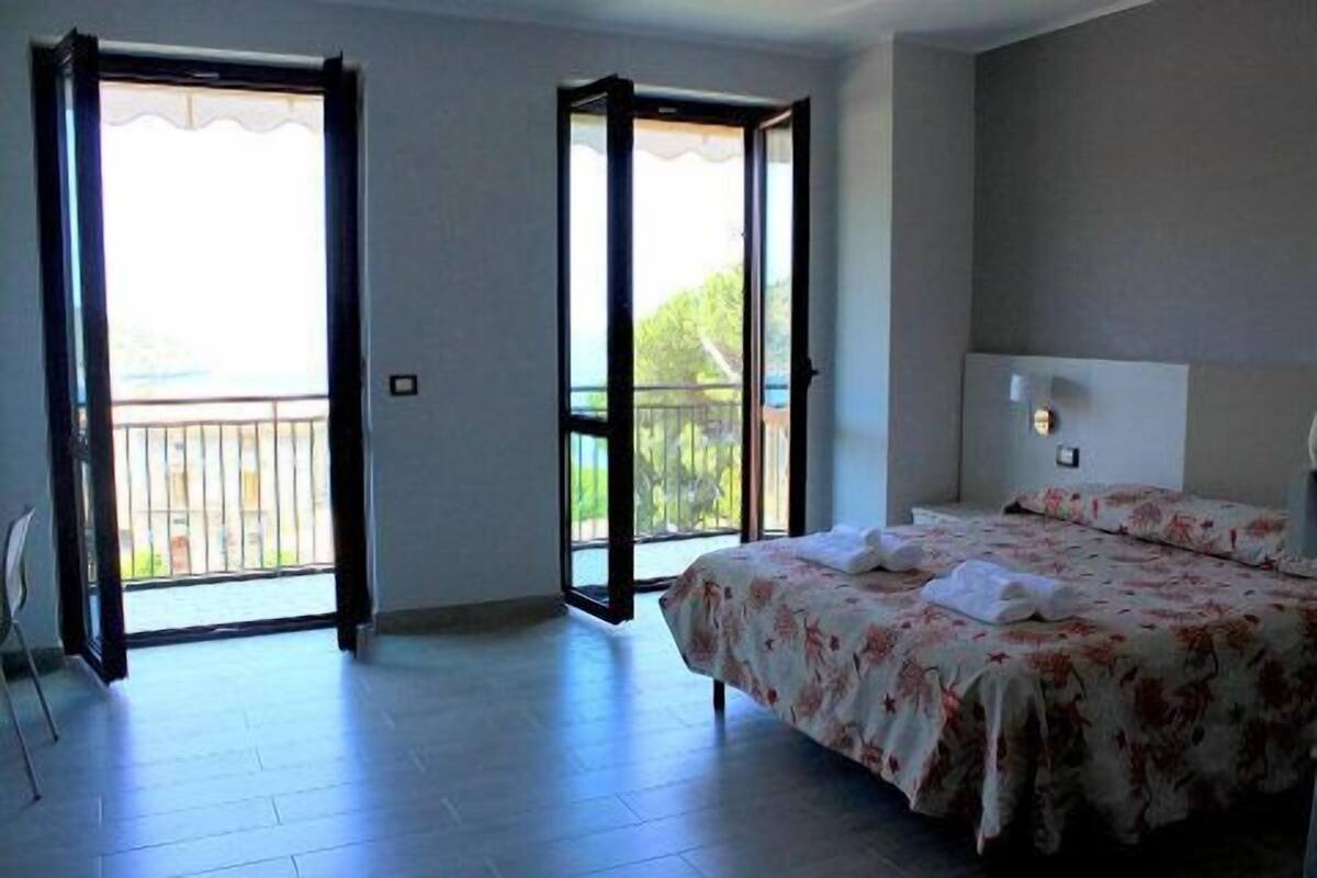 A hotel room with a bed, a nightstand, a window, and a balcony.
