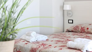 Une chambre d’hôtel avec un lit, une lampe fixée au mur et une plante en pot.