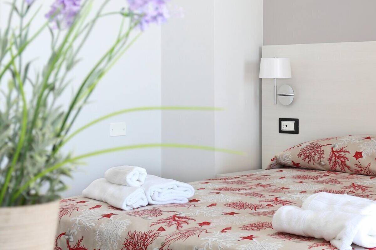 A hotel room with a bed, a wall-mounted lamp, and a potted plant.