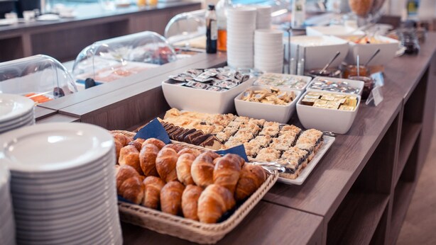 Un bufé con diversos alimentos, entre ellos pasteles y postres, dispuesto sobre una mesa de madera.