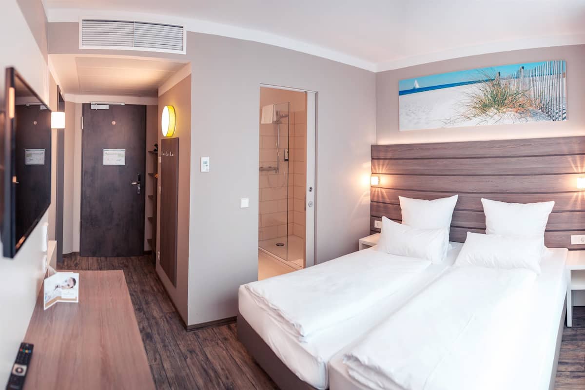 Quarto de hotel com cama, mesa de cabeceira e área de chuveiro.