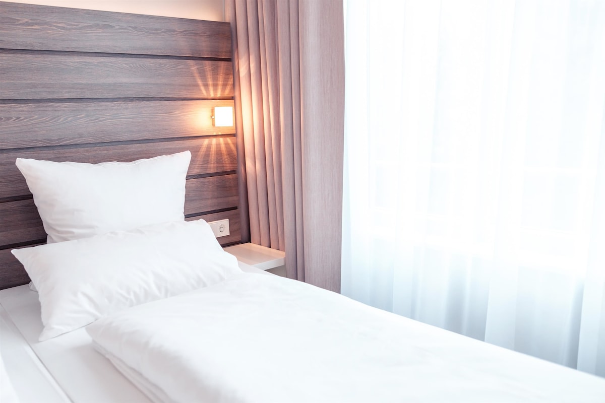 Uma cama bem arrumada com lençóis brancos, cabeceira de madeira e luminária de cabeceira.