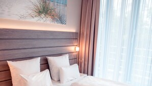 Una habitación de hotel con cabecera de madera, ropa de cama blanca y un cuadro con una playa.