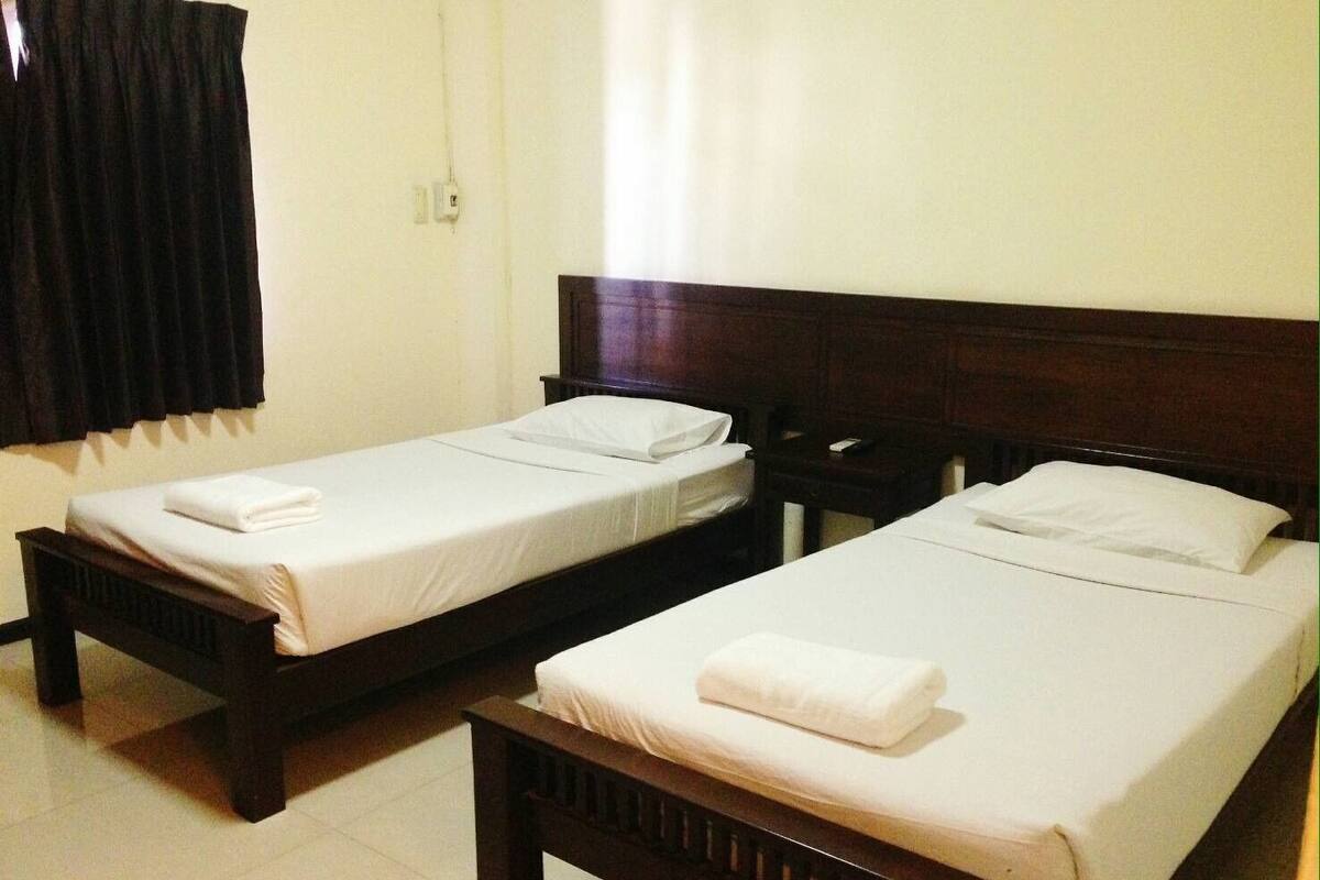 A hotel room with two single beds, each with a wooden headboard and white linens.