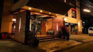 A building with a covered entrance, potted plants, and a vehicle parked outside. - Natee Place (Chiang Mai)