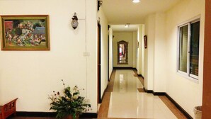 A hallway with a tiled floor, a potted plant, a framed painting, and a wall-mounted light fixture. - Natee Place (Chiang Mai)