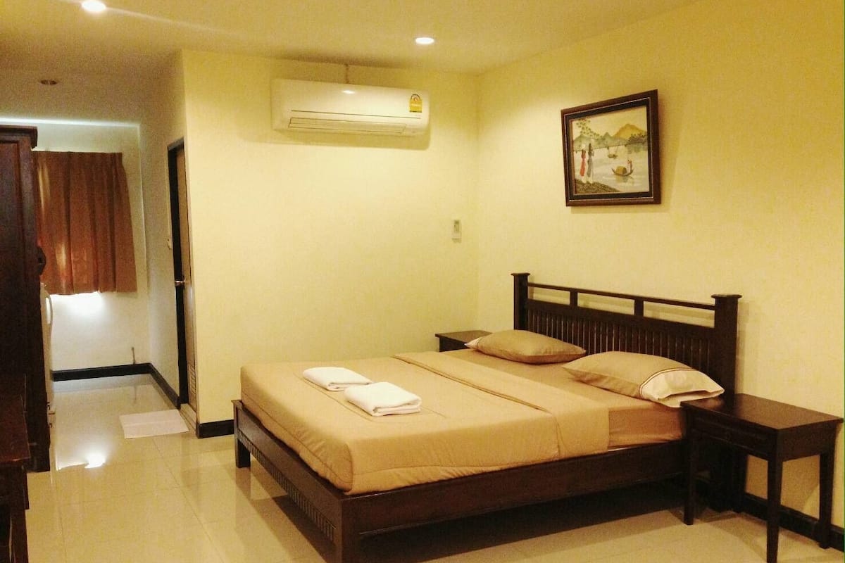 A bedroom with a wooden bed, two bedside tables, an air conditioning unit, and a framed picture on the wall.