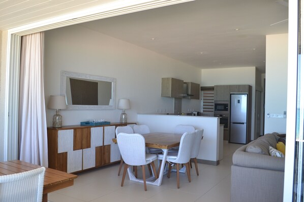 A modern kitchen with a central island, white chairs, and a wooden dining table.