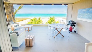 Een overdekt terras met uitzicht op het strand, straatmeubilair en een barbecue.