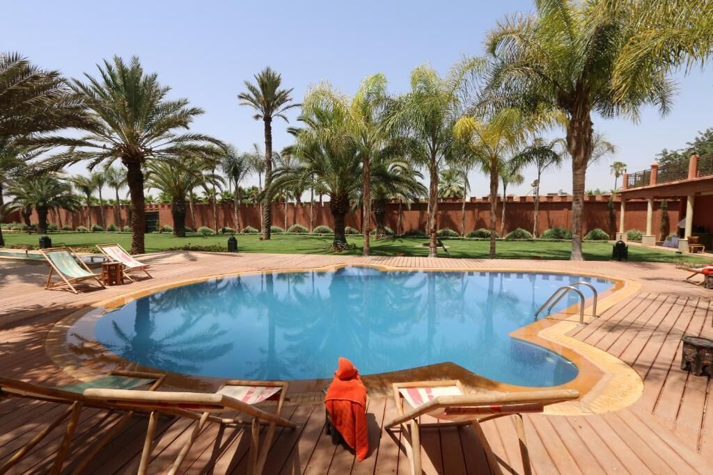 A pool area with wooden deck, lounge chairs, and palm trees.