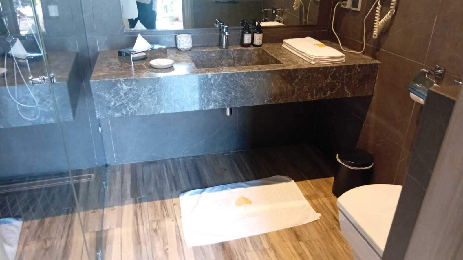 Un baño con encimera de mármol, lavamanos, espejo, inodoro y zona de ducha.