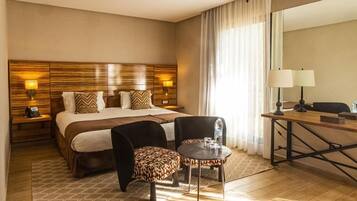 Una habitación de hotel con una cama grande, dos sillas, una mesita pequeña, un escritorio y un espejo.