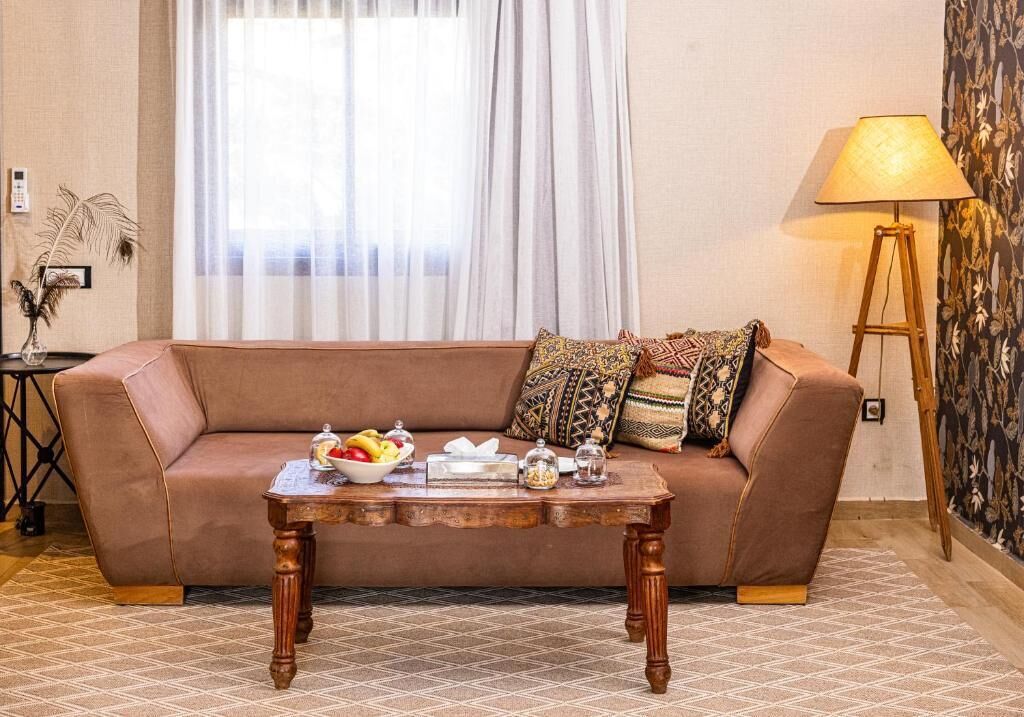 Ein Wohnzimmer mit einem braunen Sofa, einem Couchtisch mit Früchten, einer Lampe und einer Wand mit Muster.