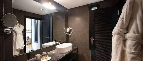 Un baño moderno con un espejo grande, un espejo redondo, un lavabo blanco y una encimera oscura.