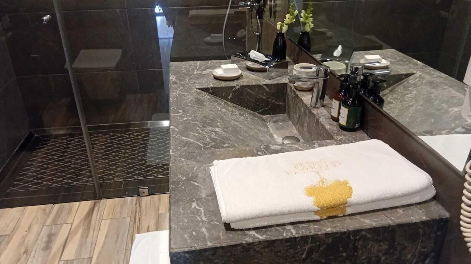 Un baño moderno con encimera de mármol, cabina de ducha de vidrio y una toalla con diseño dorado.