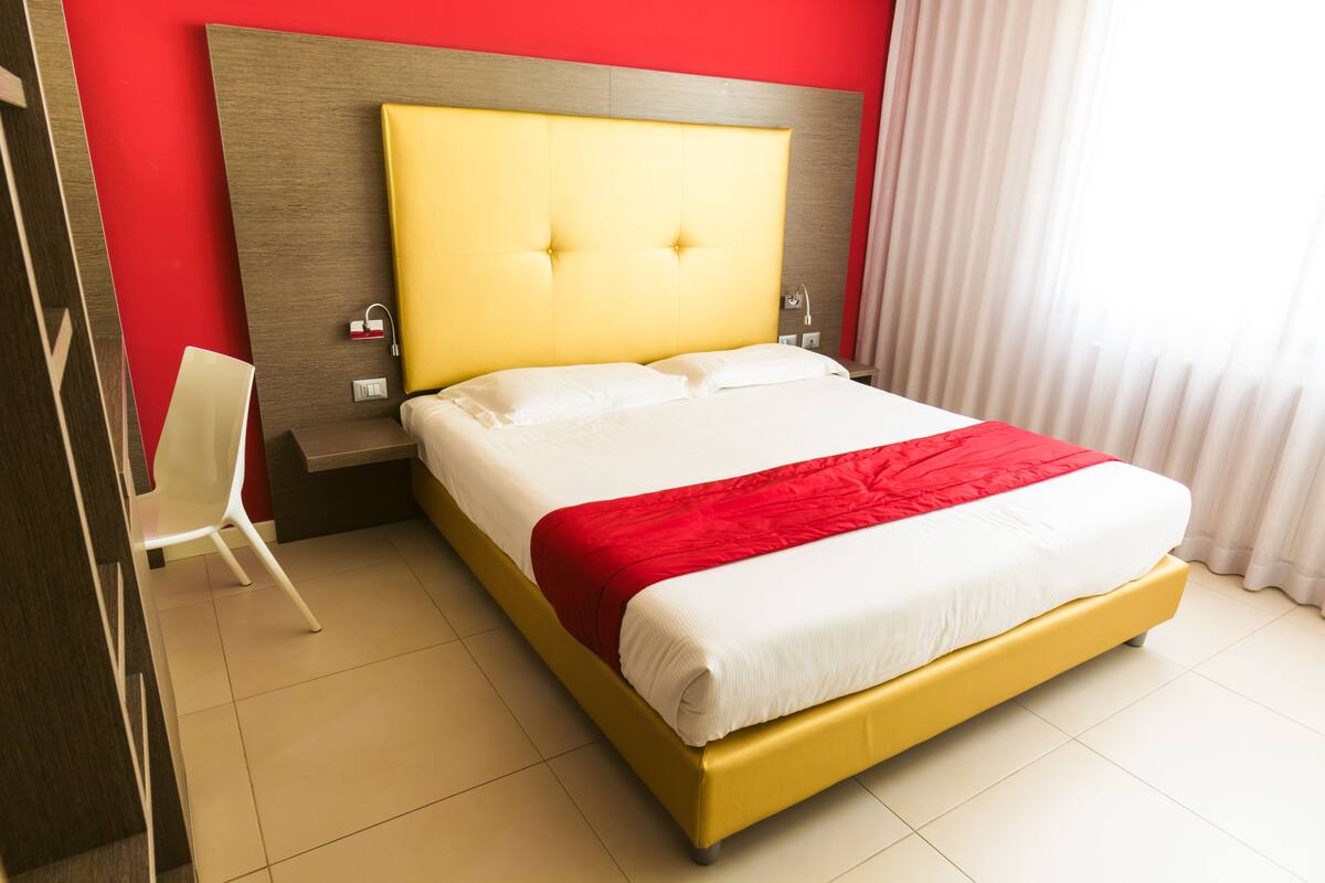 Una habitación de hotel con una cama grande, cabecera de madera, una silla blanca y una pared de acento roja.