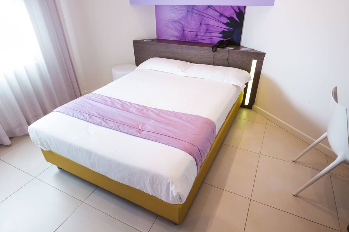 Una cama con cabecera blanca y amarilla, almohada blanca y manta morada.