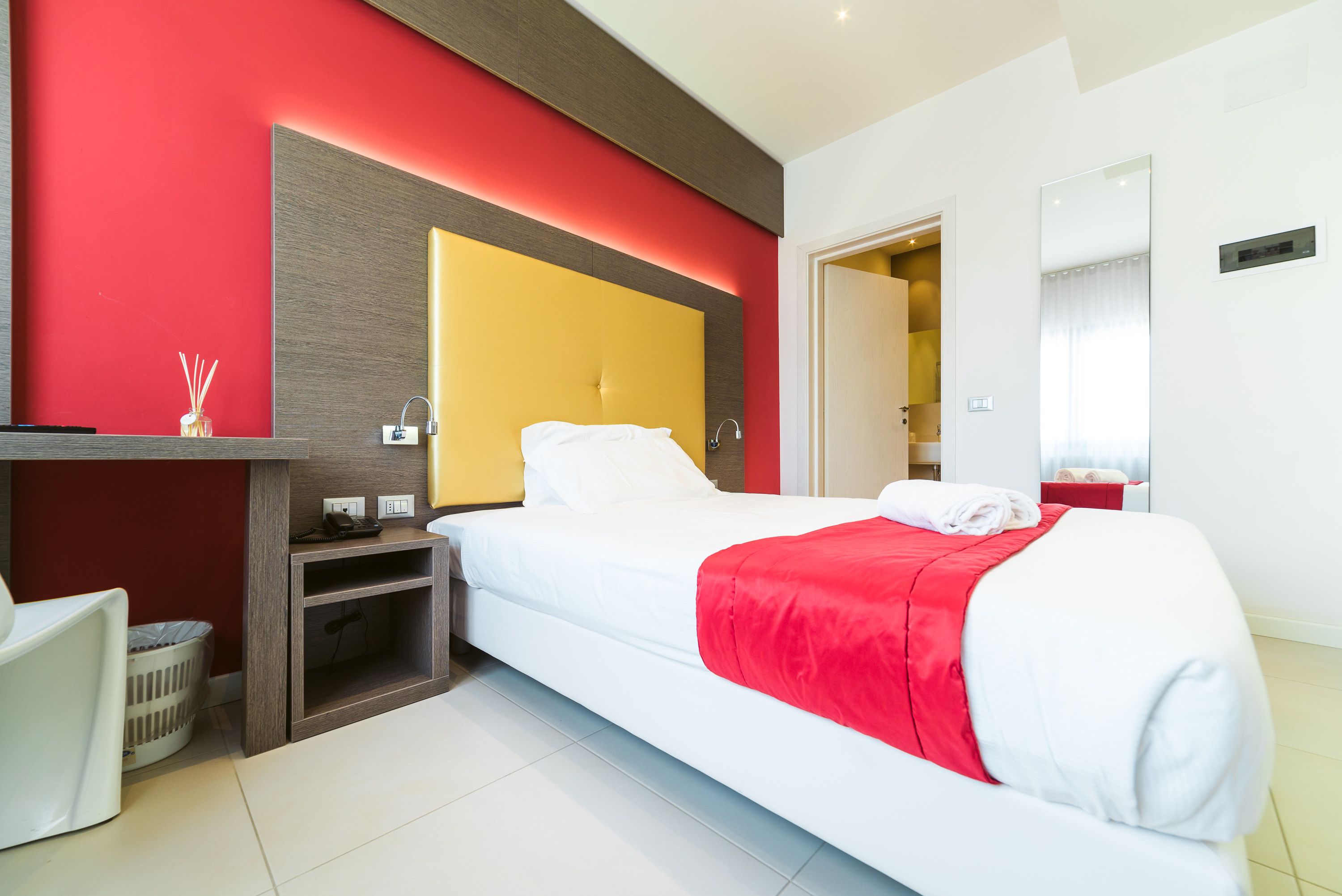 Une chambre d’hôtel avec un lit, une table de chevet et un mur d’accent de couleur rouge.