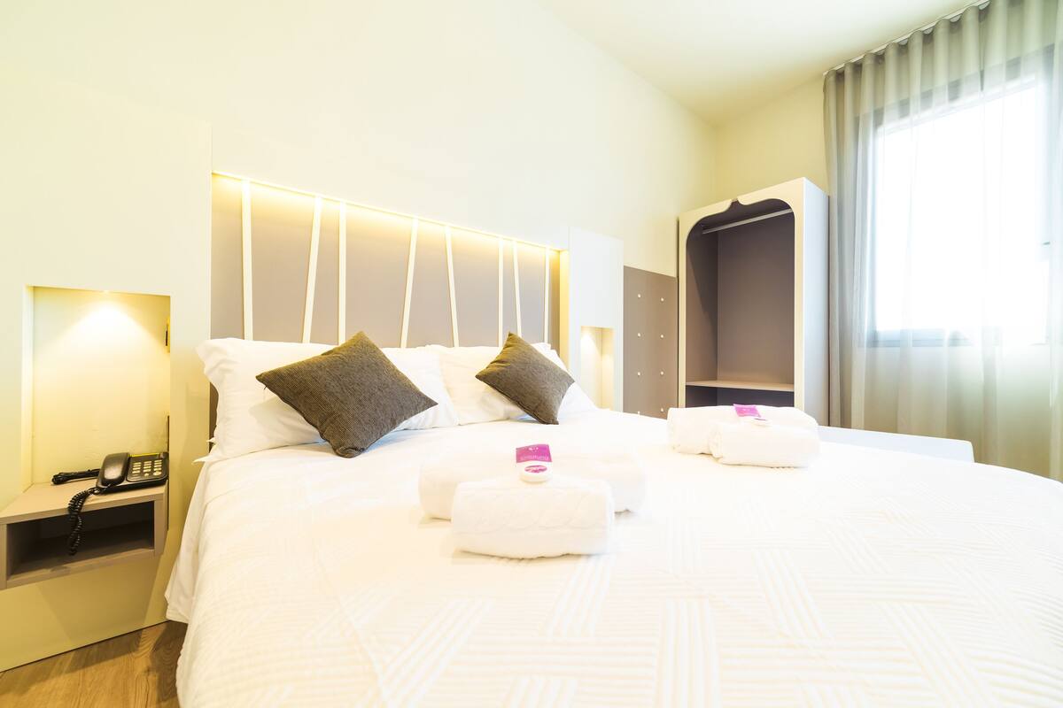 Una habitación de hotel con una cama bien hecha, un teléfono junto a la cama y un armario.
