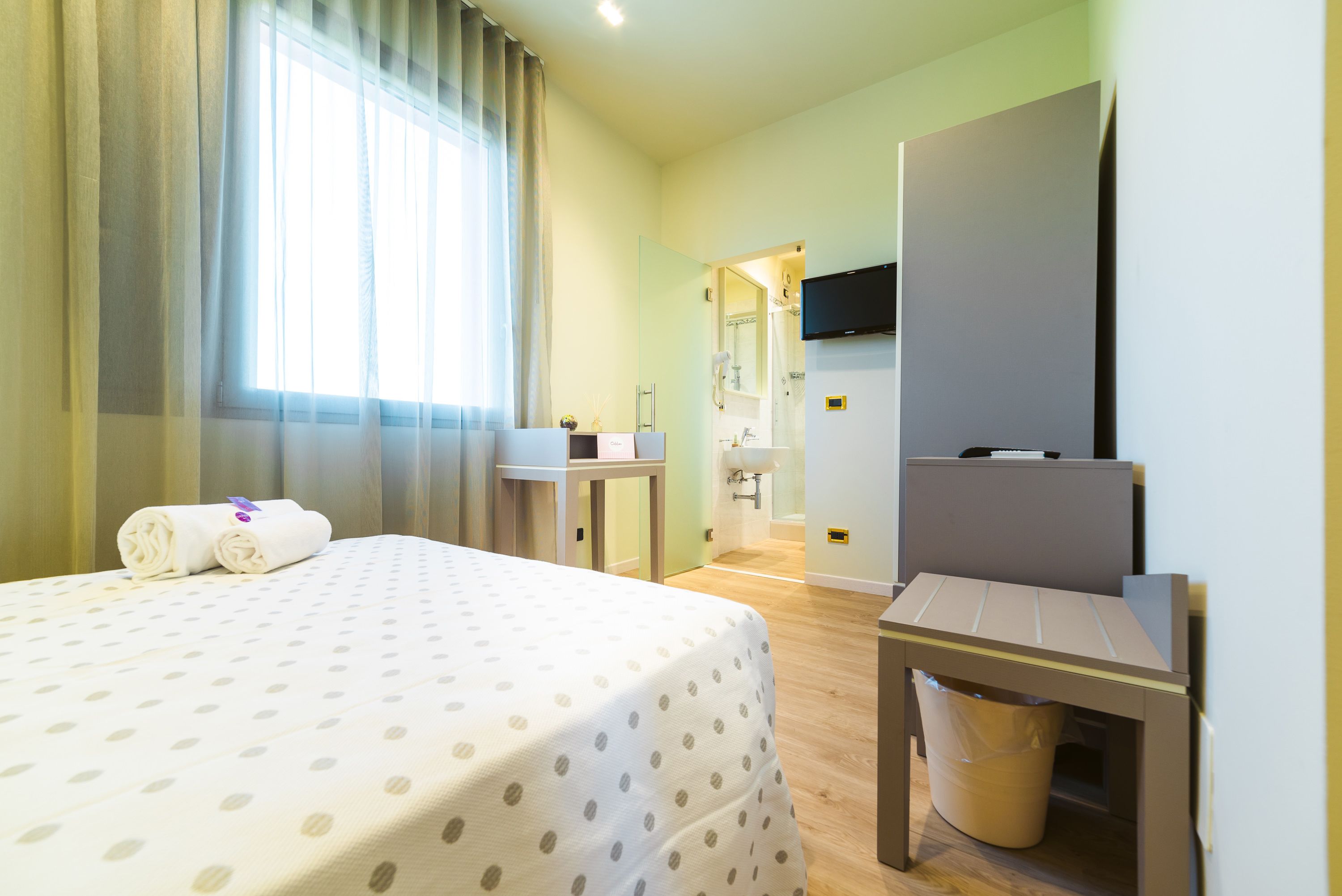 A hotel room with a bed, a desk, a chair, a TV, and a bathroom visible through an open door.