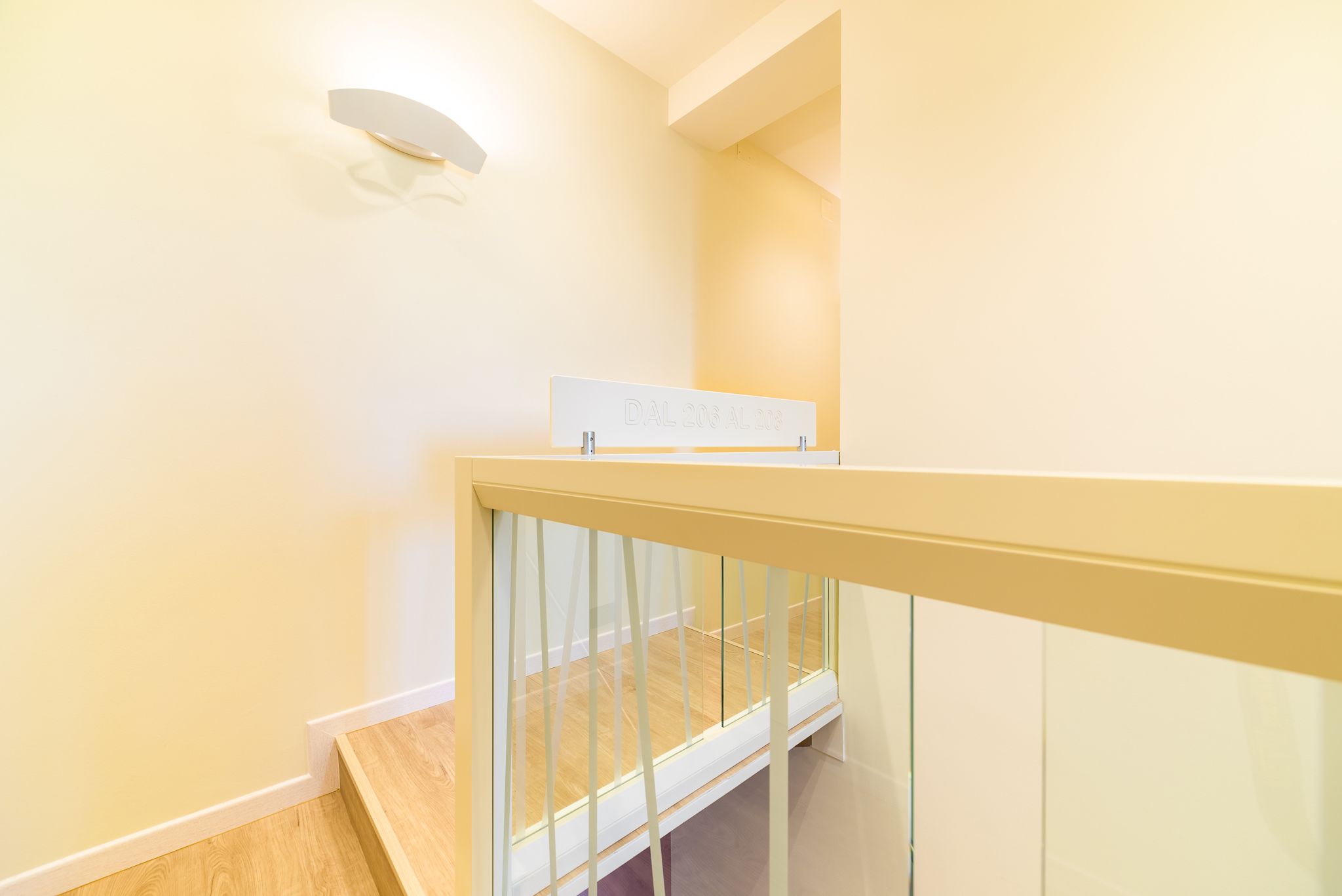 A staircase with a glass railing and a sign on the landing.