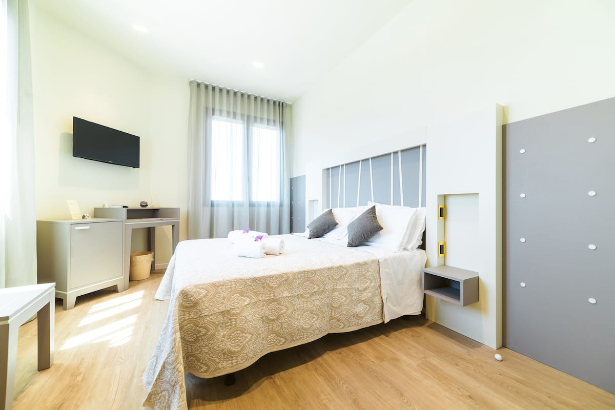 Una habitación de hotel moderna con una cama grande, un escritorio, un televisor de pantalla plana y un ventanal con cortinas.