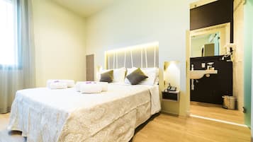 Una habitación de hotel con una cama grande, mesitas de noche, un espejo y un baño visible a través de una puerta abierta.