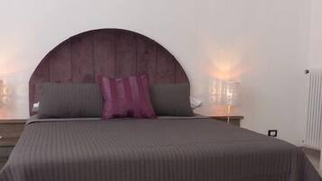 A bedroom with a bed, two bedside tables, a nightstand, a radiator, and a stool.