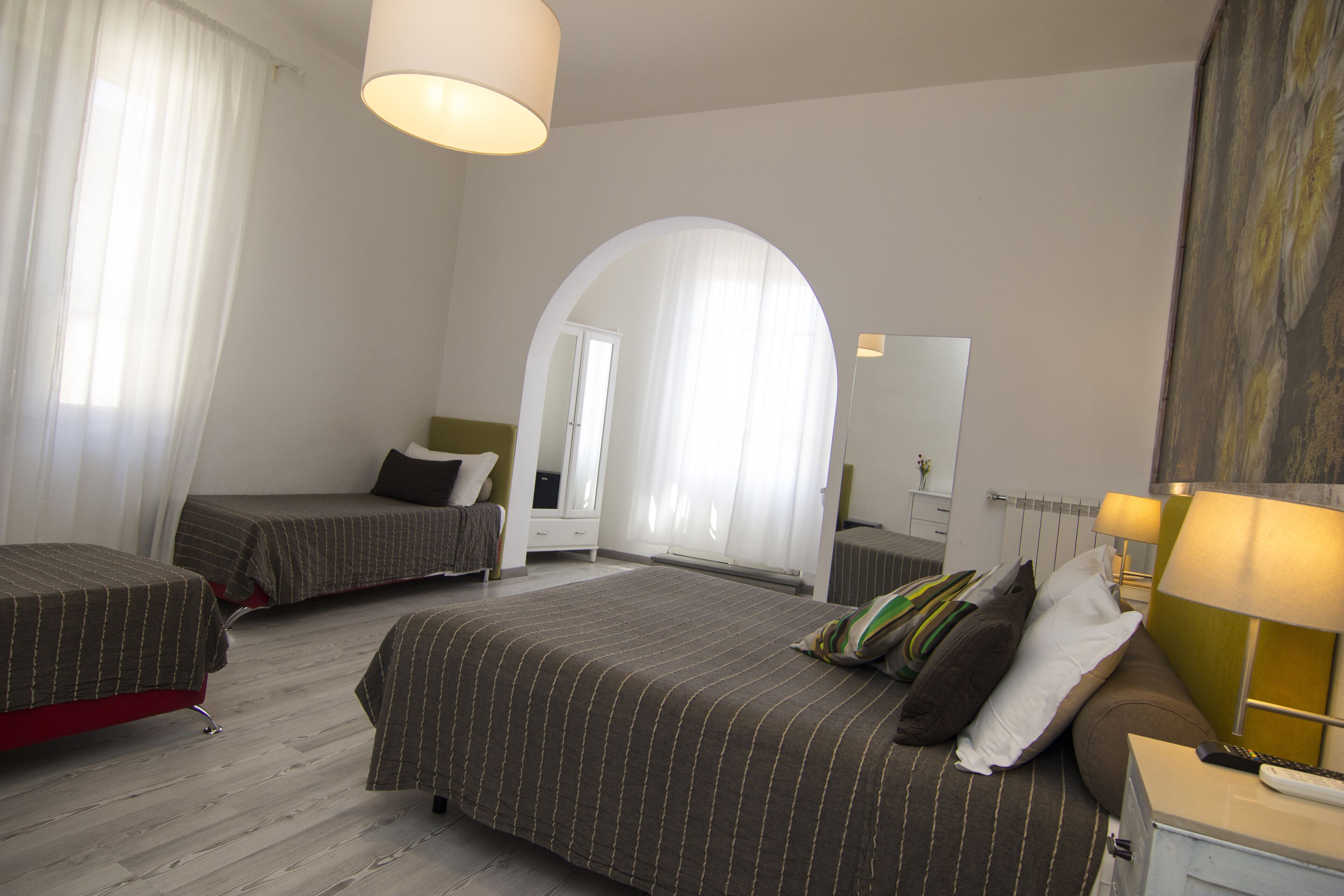 Une chambre d’hôtel avec deux lits simples, un grand miroir, un bureau avec une lampe et une vue sur le paysage urbain par la fenêtre.
