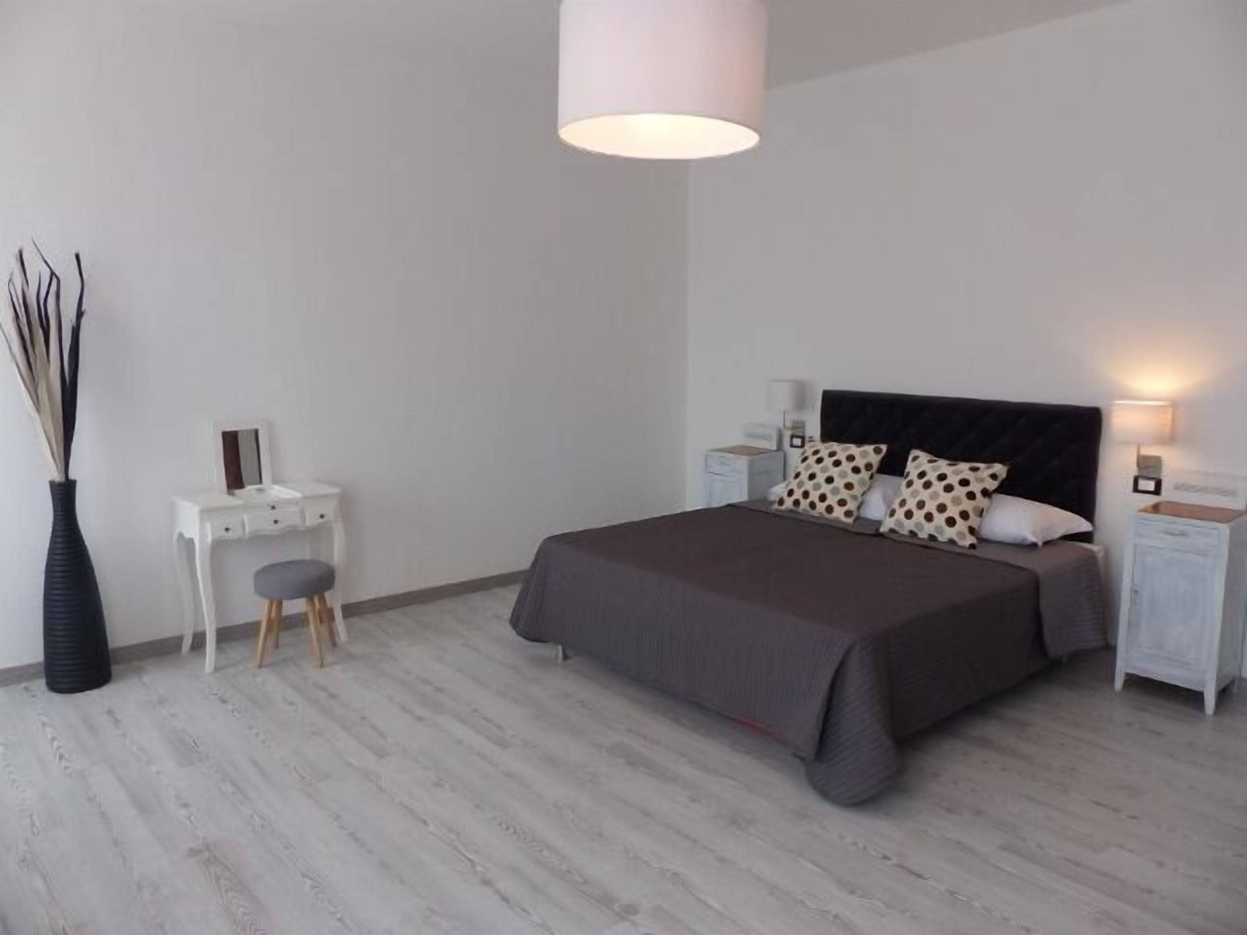 A modern bedroom with a large bed, bedside tables, a dresser, and a hanging light fixture.