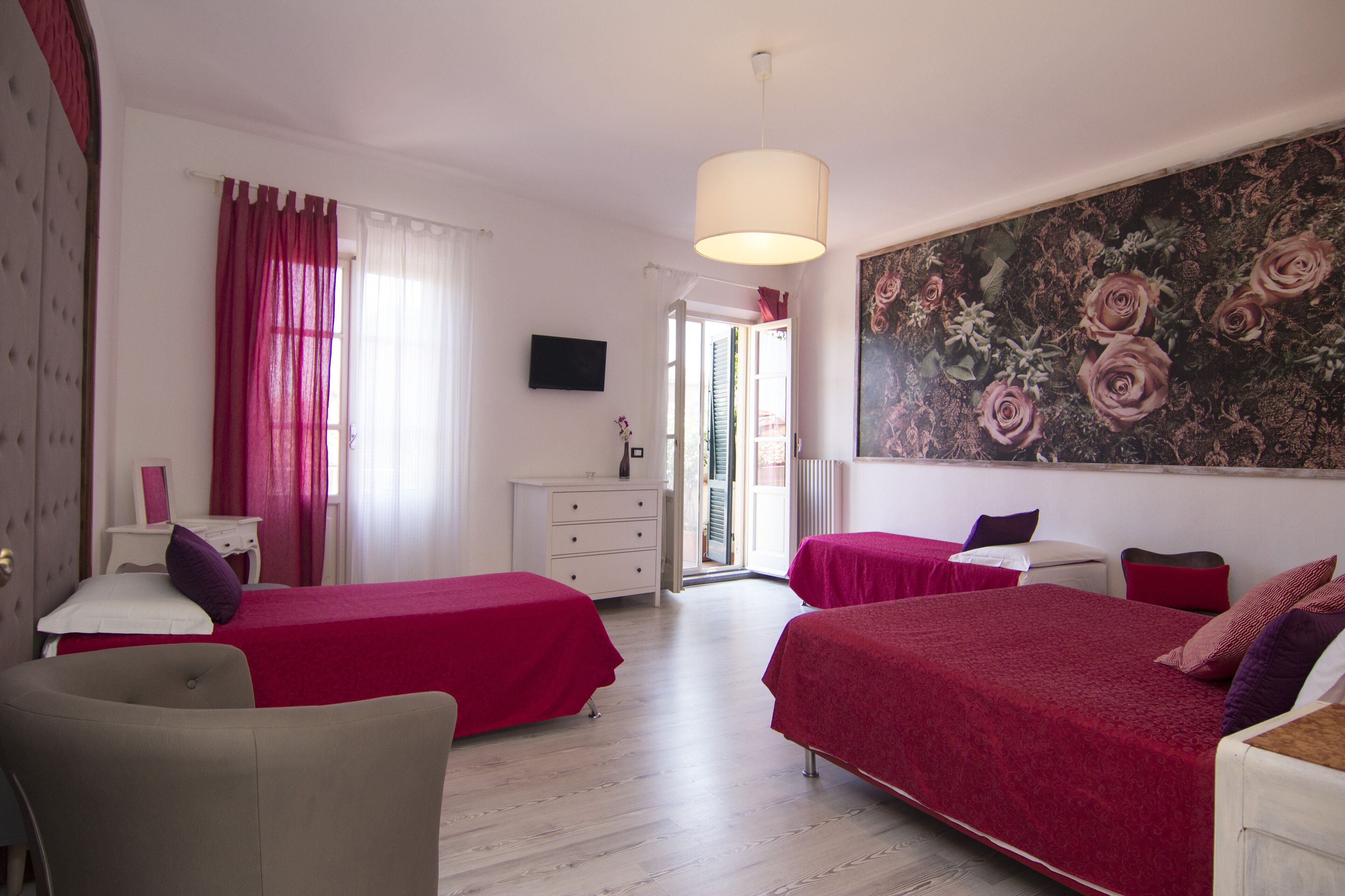 A hotel room with two beds, a large floral artwork on the wall, a television, and a view of the outside.