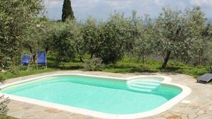 A swimming pool with a stone border, surrounded by lounge chairs and a view of the countryside.