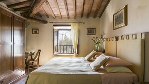 A bedroom with a wooden ceiling, a bed with a beige bedspread, a chair, and a window with curtains.