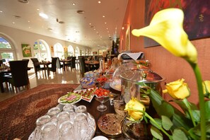 Un comedor con mesas dispuestas para un bufé, mostrando diversas opciones de comida y cristalería.
