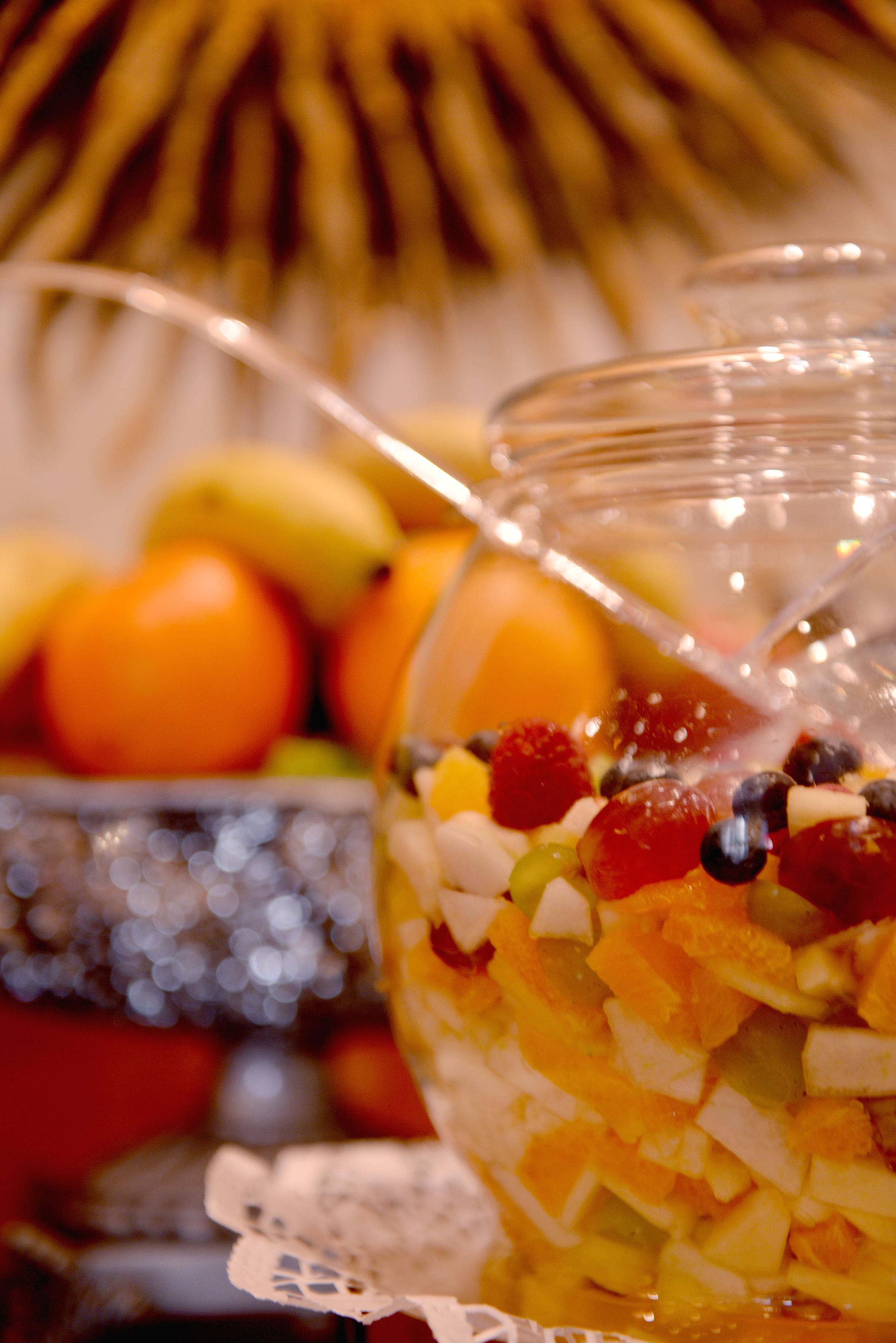 A bowl of fruit salad with a spoon in it, placed on a table with a decorative doily.