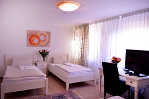 Ein Hotelzimmer mit zwei Einzelbetten, einem Schreibtisch mit Fernseher und einem Fenster mit durchscheinenden Vorhängen.