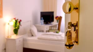 Habitación de hotel con cama, mesita de noche, televisor y escritorio con silla. Hay una puerta con cerradura de tarjeta.