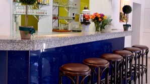 Una zona de bar con una encimera azul, varios taburetes y una estantería con botellas y vasos.