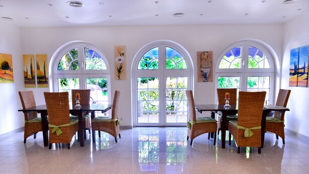 Un comedor con suelo pulido, ventanas arqueadas amplias y sillas de mimbre con cojines verdes.