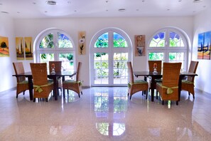 A dining area with a polished floor, large arched windows, and wicker chairs with green cushions. - Alpha Hotel Garni (Dietzenbach)