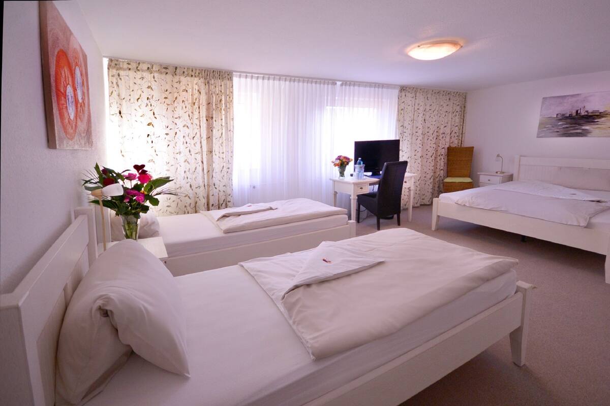 A hotel room with two single beds, a desk with a chair, a television, and a painting on the wall.