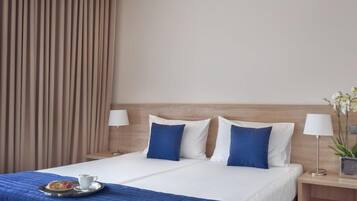 Habitación de hotel con cama, dos mesitas de noche, lámpara, bandeja con una taza y un pastel, y cortina.