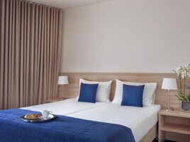 Habitación de hotel con cama, dos mesitas de noche, lámpara, bandeja con una taza y un pastel, y cortina.