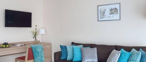 Una sala de estar con un sofá marrón, un escritorio de madera, una silla, un televisor y un cuadro en la pared.