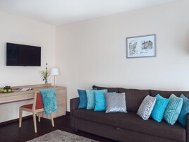 Una sala de estar con un sofá marrón, un escritorio de madera, una silla, un televisor y un cuadro en la pared.