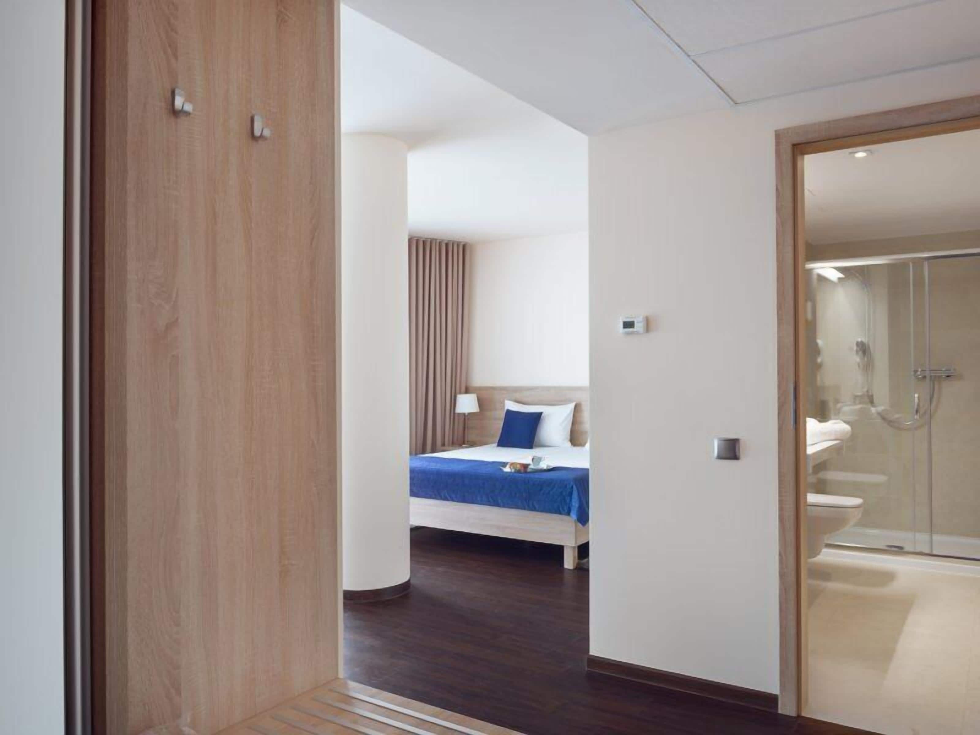 Una habitación de hotel con cama, mesita de noche, lámpara y zona de ducha.