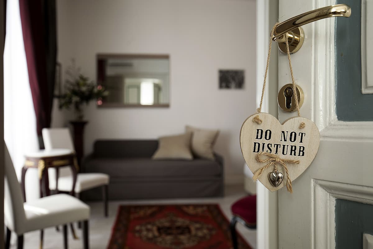 Ein Zimmer mit einem Bett, einem Sessel, einem Teppich und einer Tür mit einem 'Bitte nicht stören'-Schild.